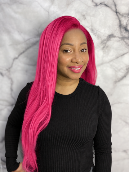 A woman with long, vibrant hot pink synthetic hair wearing a black ribbed long-sleeve top, posing against a gray and white marble-patterned background.